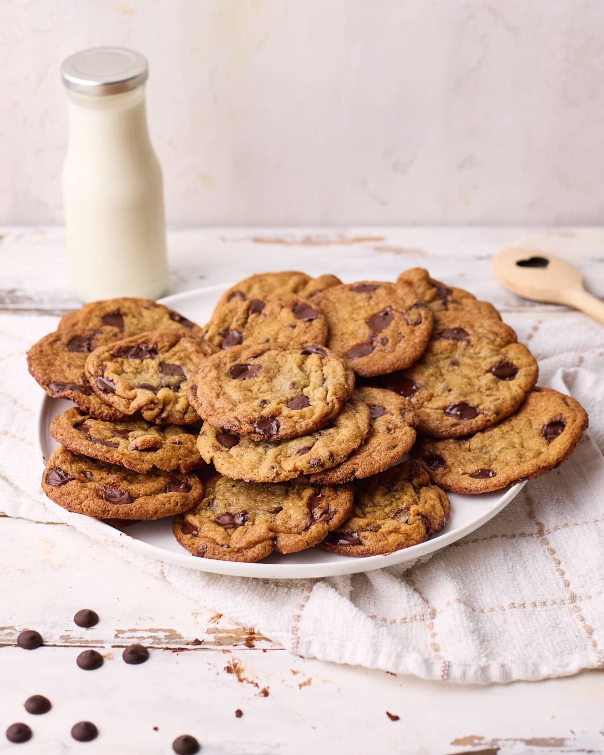 Big pile of brown butter chocolate chip cookies on a plate with a bottle of milk in the background.