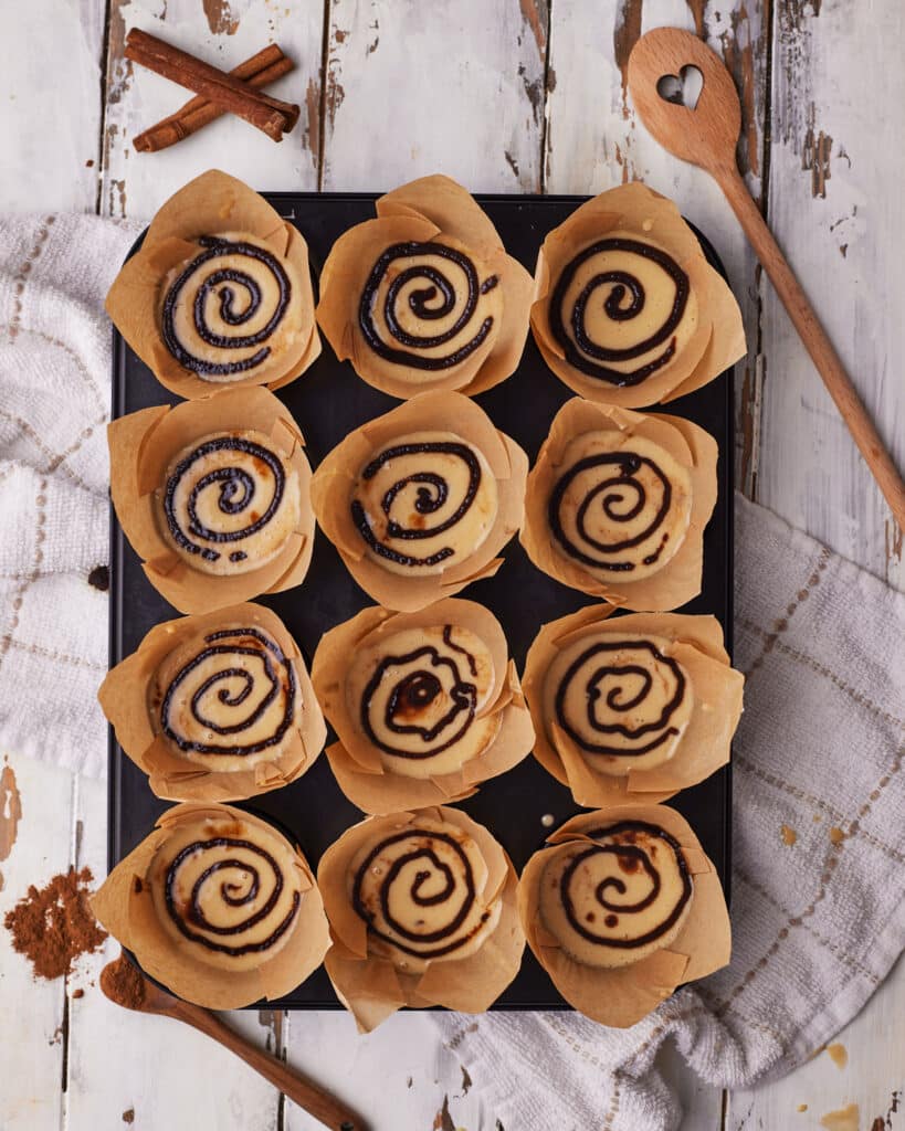 Process shots of making cinnamon roll muffins - piping cinnamon sugar swirl on top.