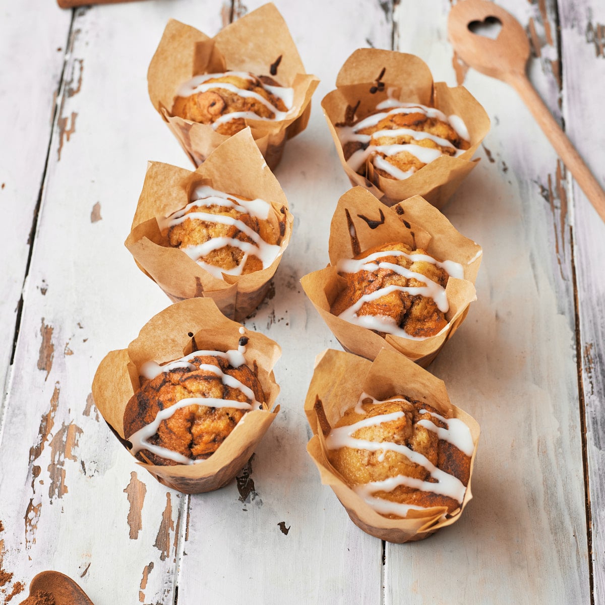 Six cinnamon roll muffins sitting on top of a rustic looking table. 