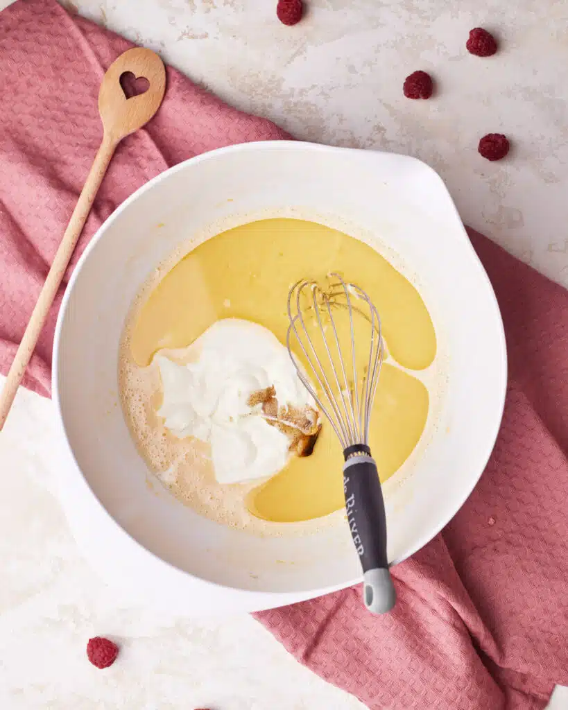 Adding sour cream, vegetable oil and vanilla to raspberry muffin batter.