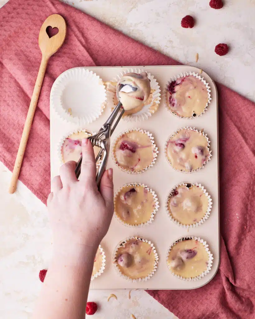 scooping raspberry muffin batter into paper liners.