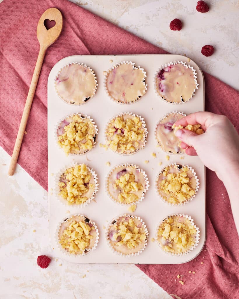 sprinkling crumb topping on top of raspberry muffins.