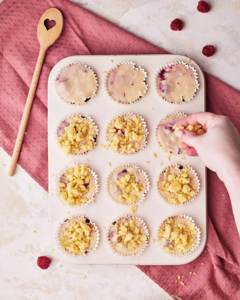 sprinkling crumb topping on top of raspberry muffins.