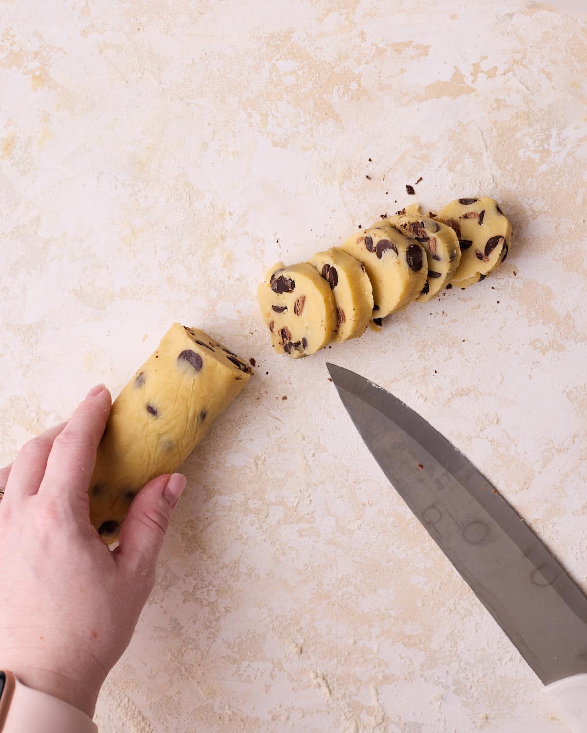 Slicing a chilled log of chocolate chip shortbread dough before baking.