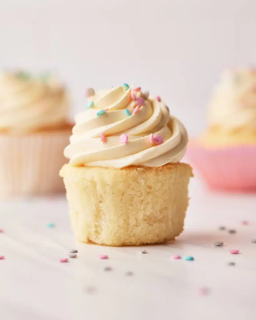Vanilla cupcakes on a table surrounded by confetti sprinkles.