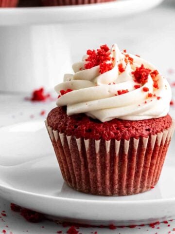 Red velvet cupcake on a plate with cream cheese frosting piped in a swirl on top.