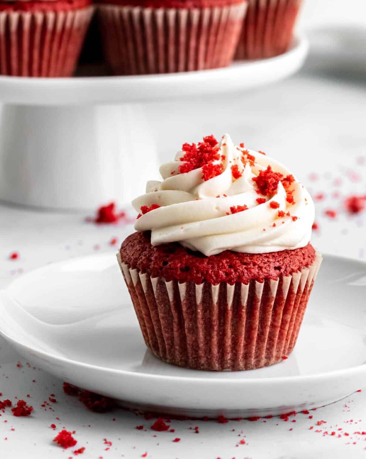 Red velvet cupcake on a plate with cream cheese frosting piped in a swirl on top.l 