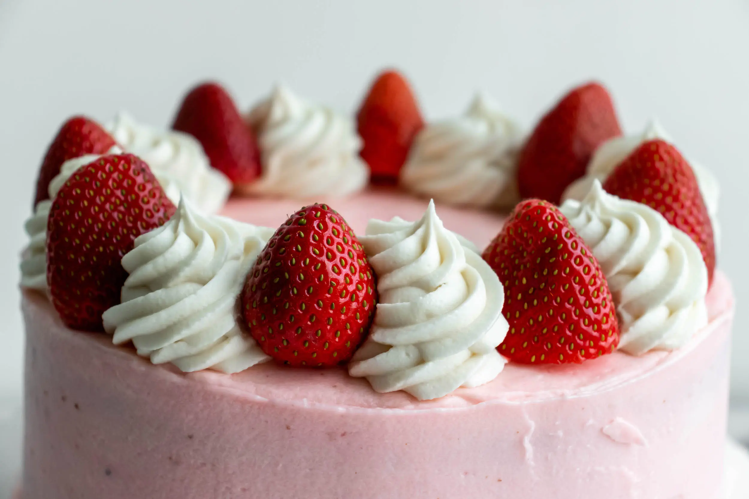 An up close view showing the top of the fully decorated strawberry cake, with cream cheese frosting swirls, with strawberries in between each swirl.