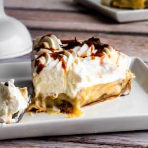 Slice of traditional banoffee pie with caramel filling, fresh banans and whipped cream, the banana infused caramel filling is drizzling out just slightly.