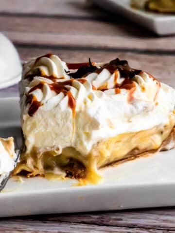 Slice of traditional banoffee pie with caramel filling, fresh banans and whipped cream, the banana infused caramel filling is drizzling out just slightly.