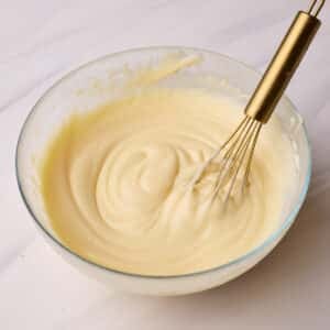 Pastry cream (creme patissiere) in a glass bowl with a small gold whisk sitting in it.