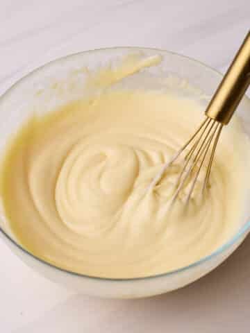 Pastry cream (creme patissiere) in a glass bowl with a small gold whisk sitting in it.