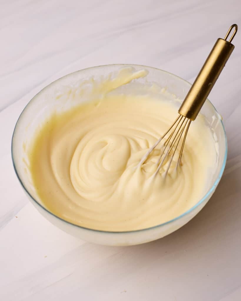 Pastry cream (creme patissiere) in a glass bowl with a small gold whisk sitting in it.