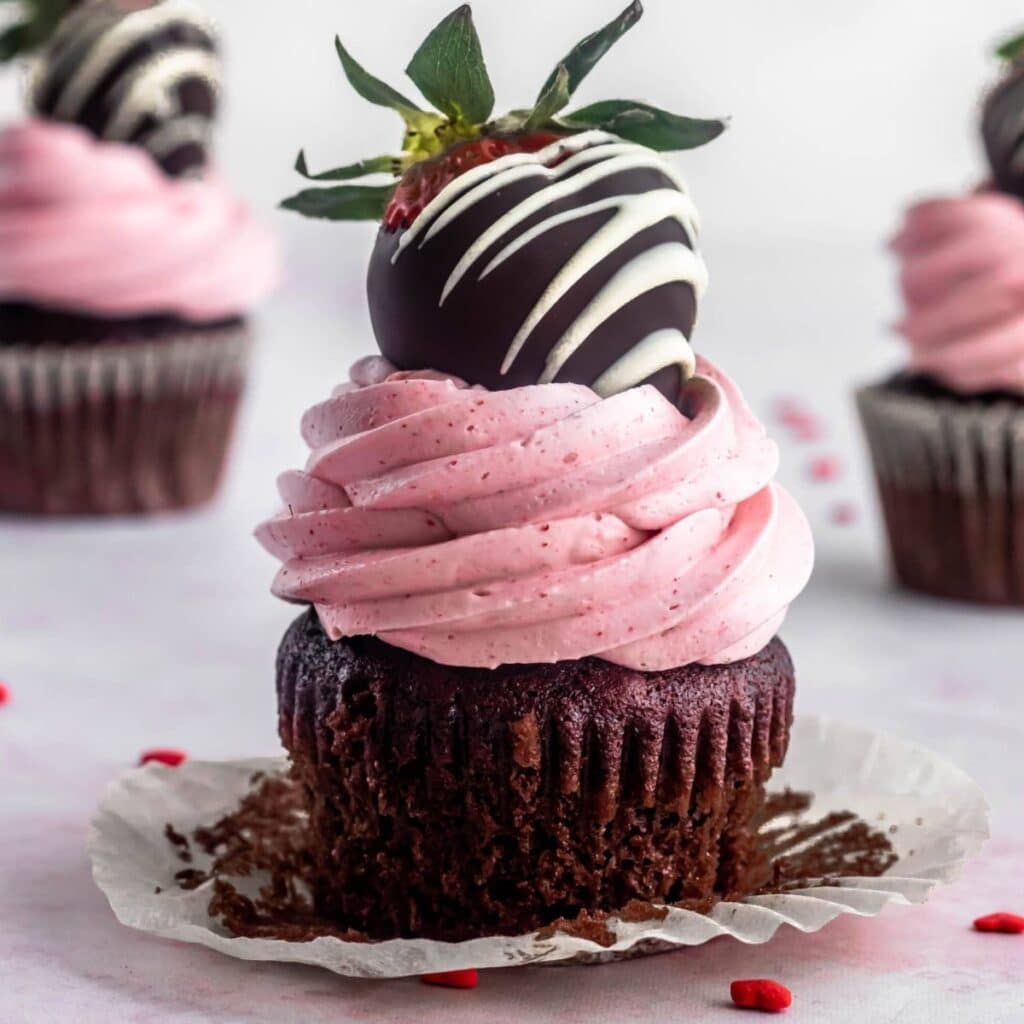 chocolate and strawberry cupcake with strawberry italian meringue buttercrem and a chocolate dipped strawberry on top.