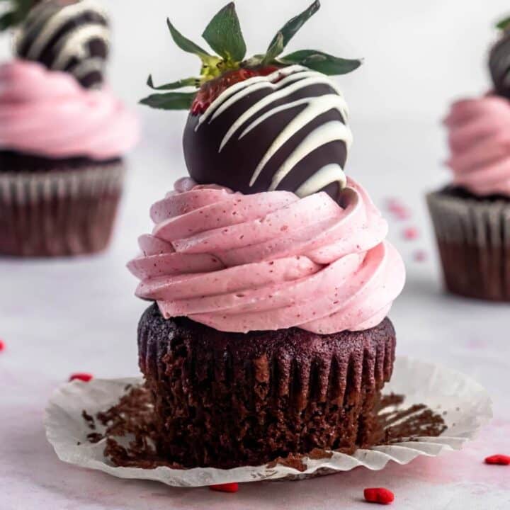 chocolate and strawberry cupcake with strawberry italian meringue buttercrem and a chocolate dipped strawberry on top.