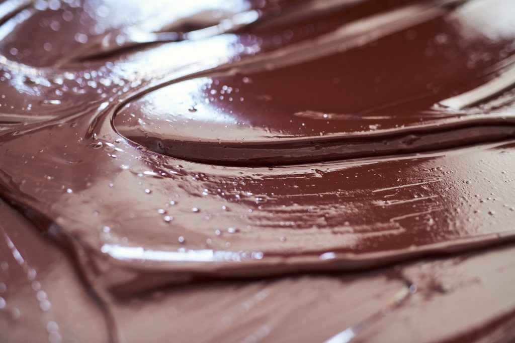 Closeup of shiny melted chocolate spread out on a table to cool in an artisanal chocolate making factory