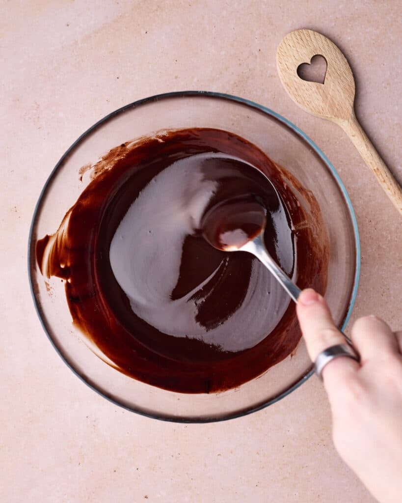 Melted chocolate and butter in a mixing bowl, being stirred together into a smooth, glossy mixture.
