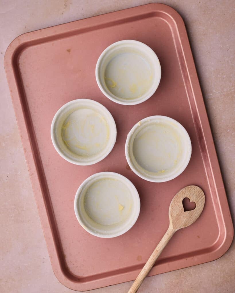 Ramekins coated in butter and sugar, on a baking sheet, ready to make chocolate lava cakes.