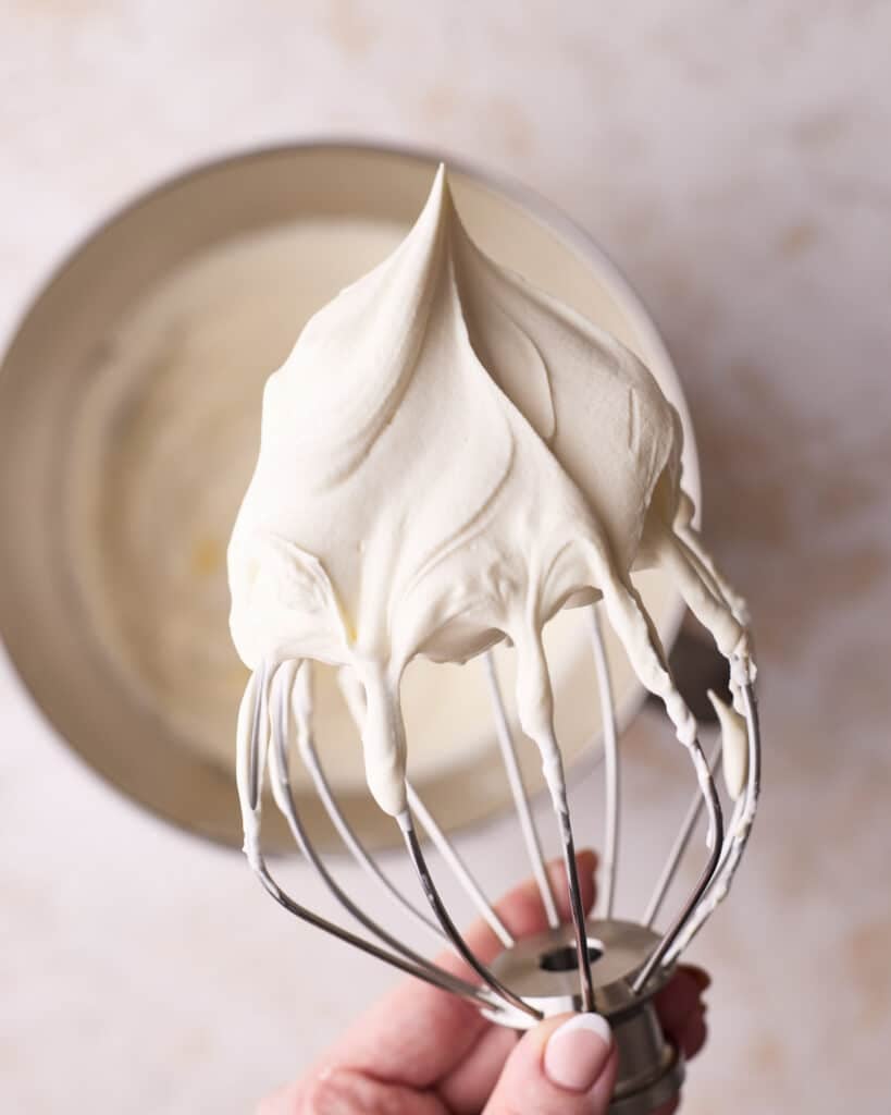 Whipped cream on a whisk, above a bowl. 