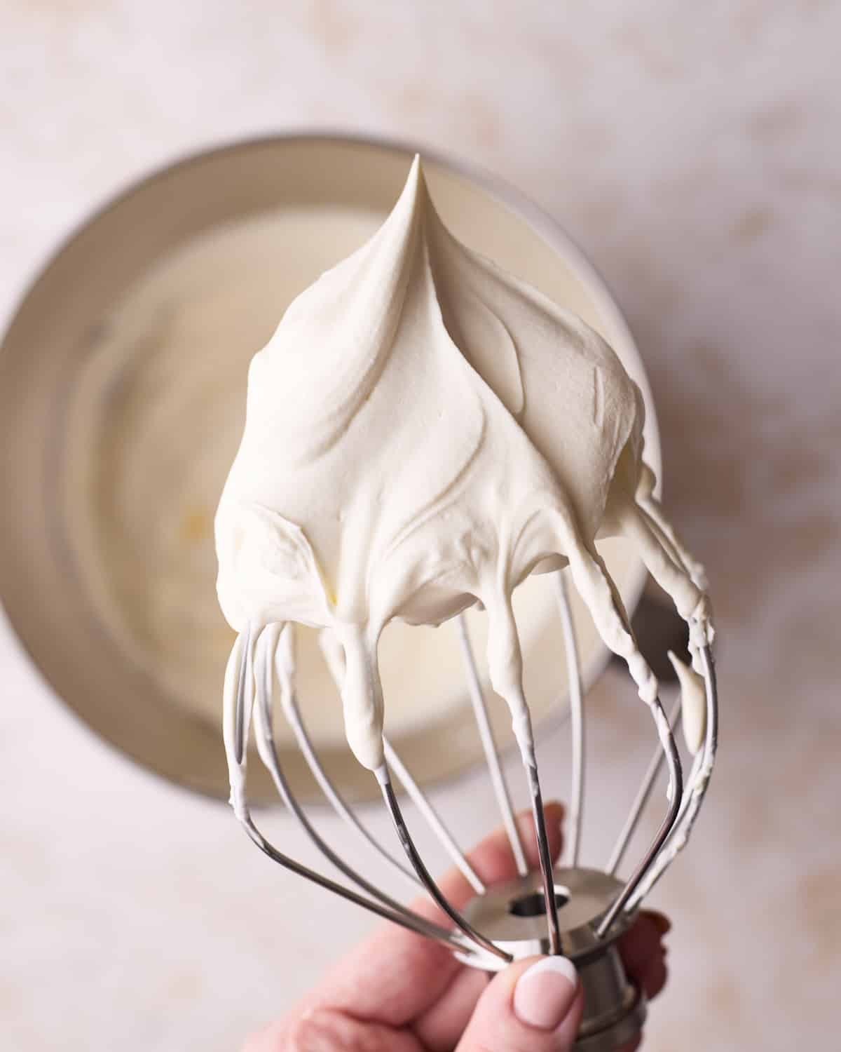 Whipped cream on a whisk, above a bowl.
