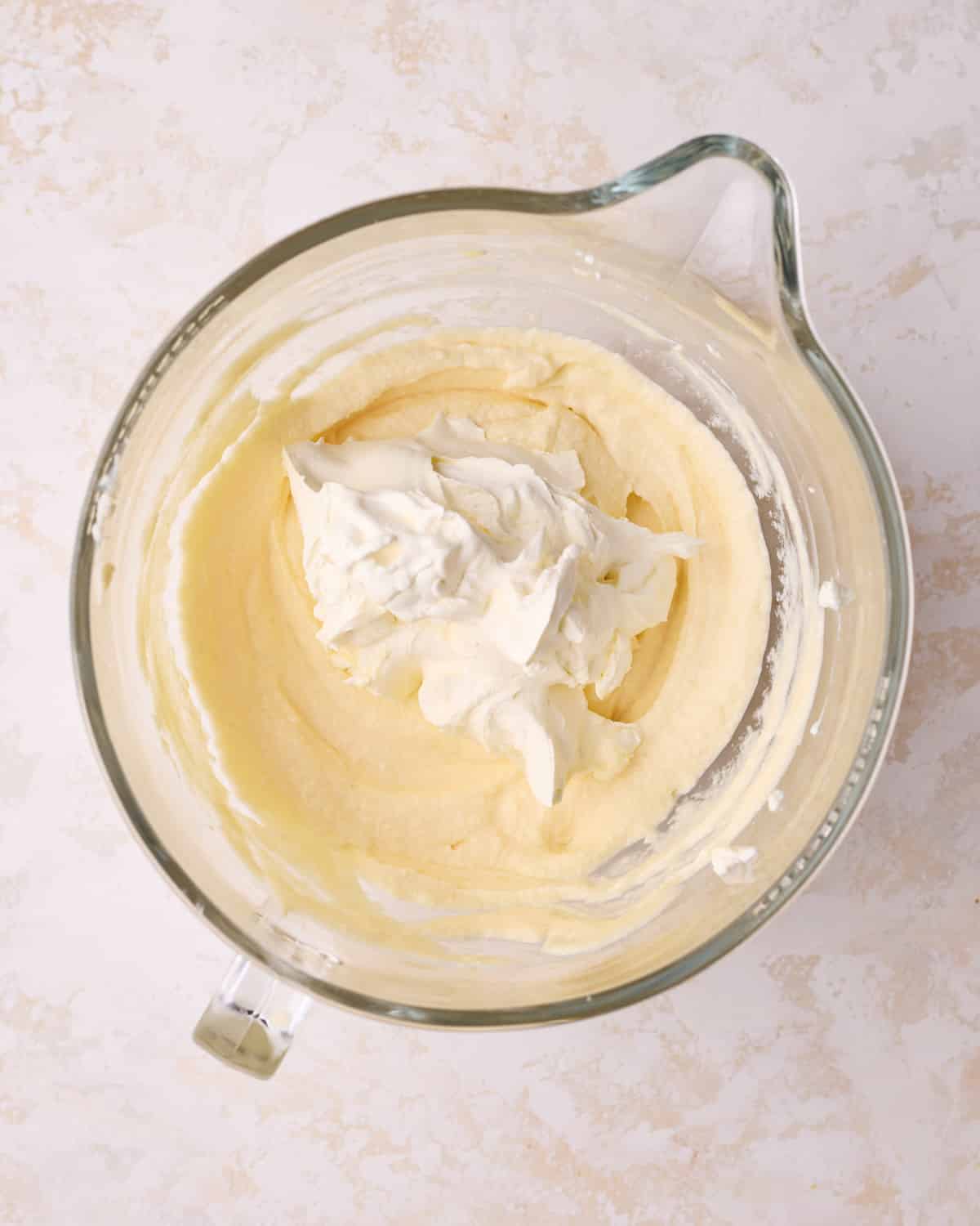 Folding whipped cream into mascarpone mixture to make filling for tiramisu cake.
