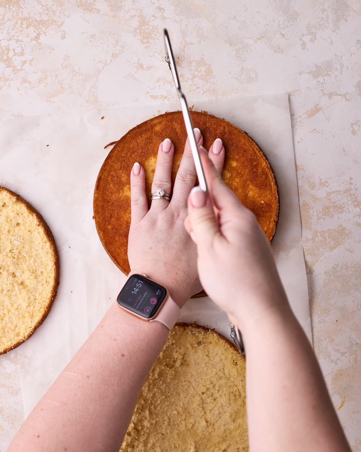 Sponge cake being sliced into thin layers with a cake leveler.
