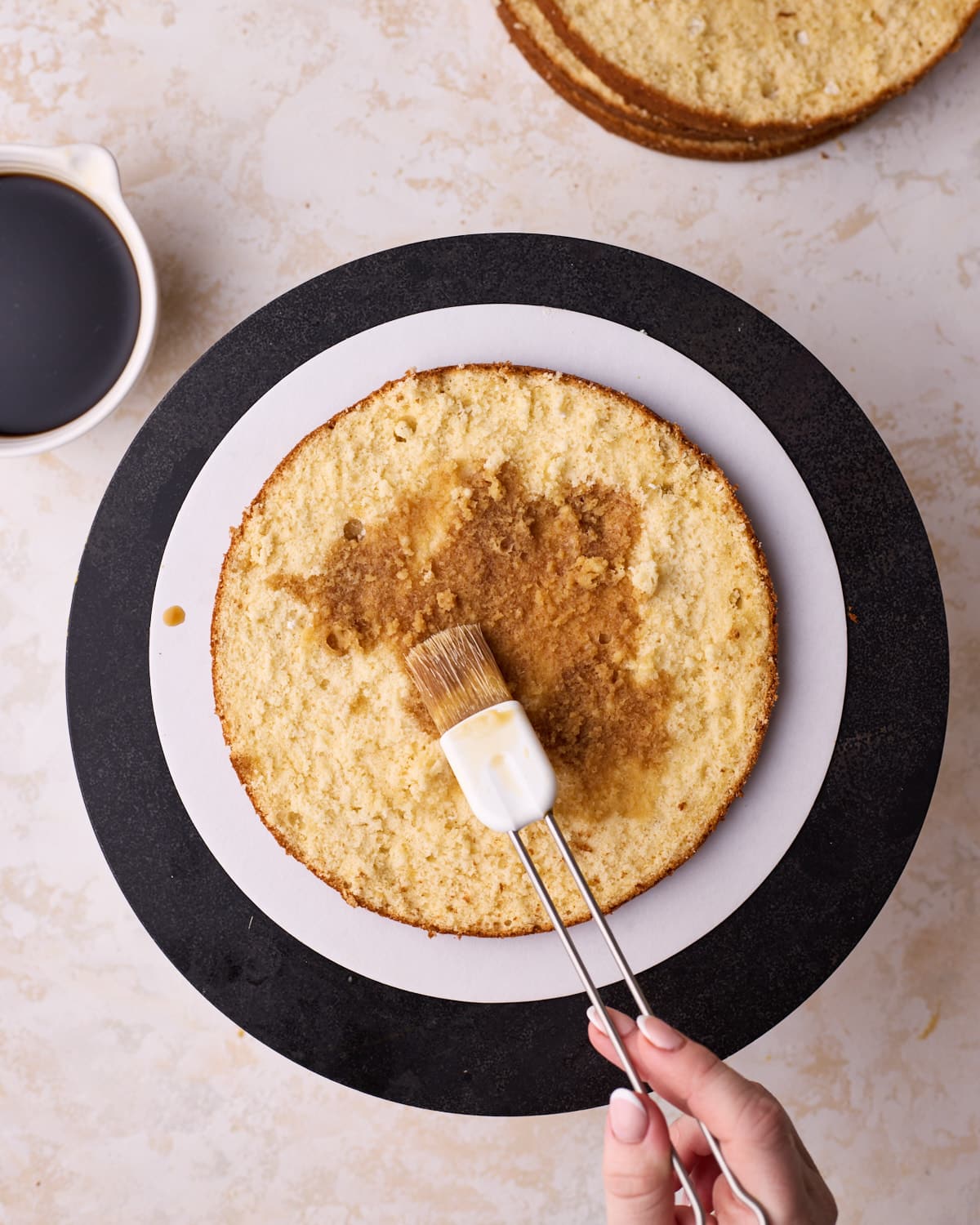Layer of genoise sponge cake being soaked with espresso soak using a pastry brush to make tiramisu cake. 