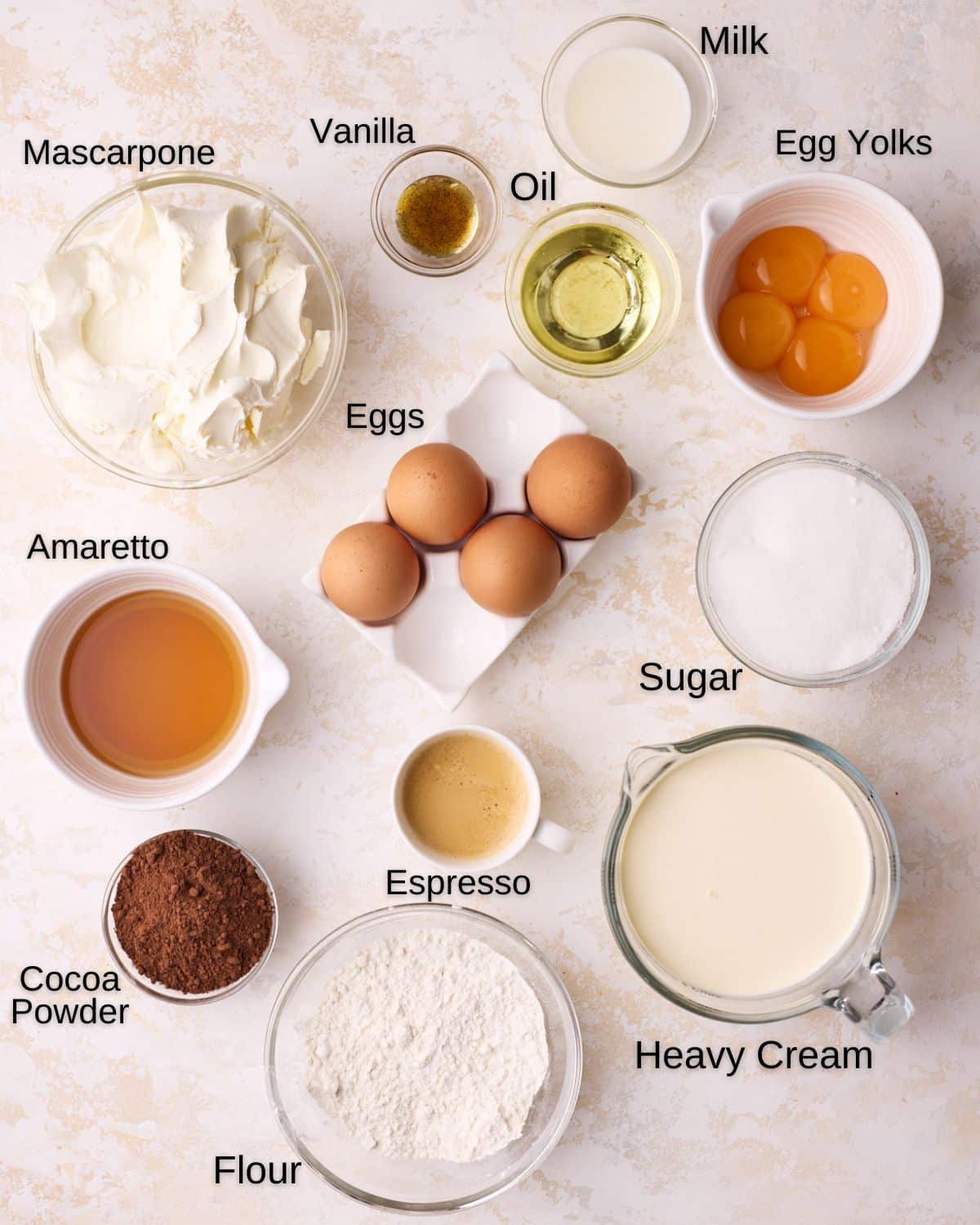 Ingredients to make tiramisu cake - eggs, cake flour, sugar, heavy cream, vanilla, oil, milk, amaretto, espresso, mascarpone, egg yolks. 