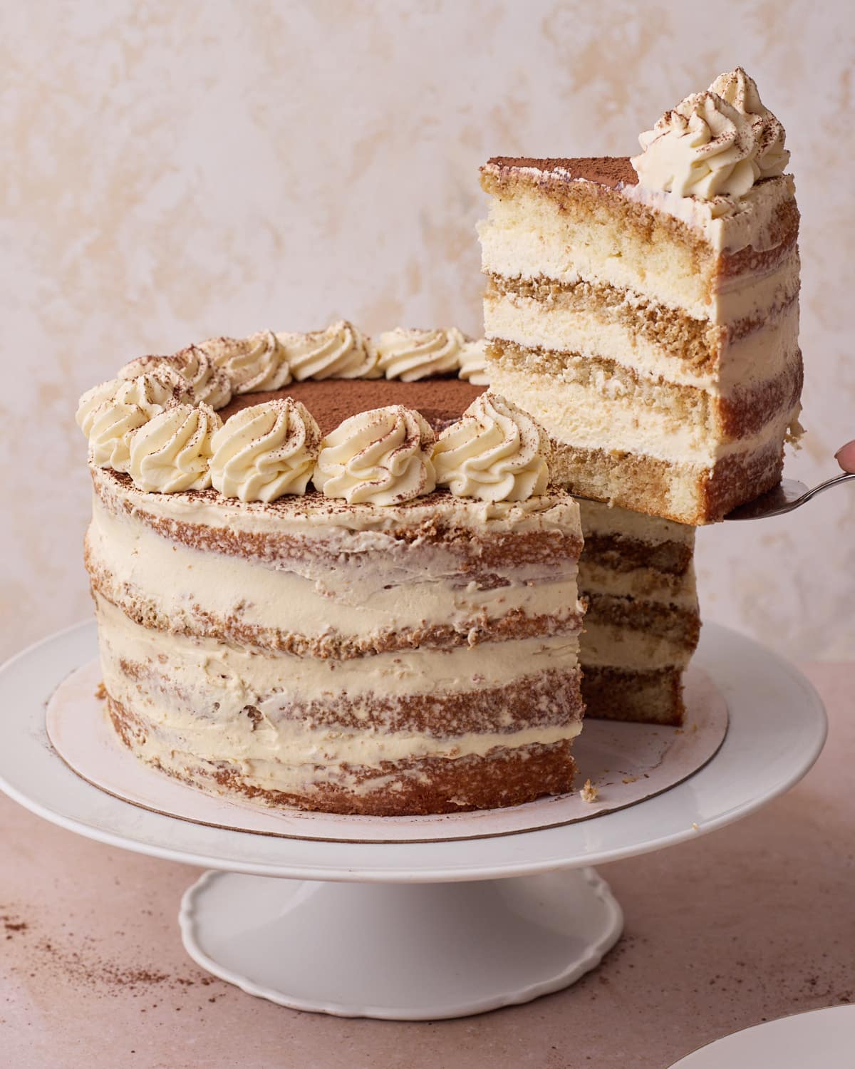 Tiramisu layer cake with a slice being lifted out of it to reveal the distinct layers inside. 