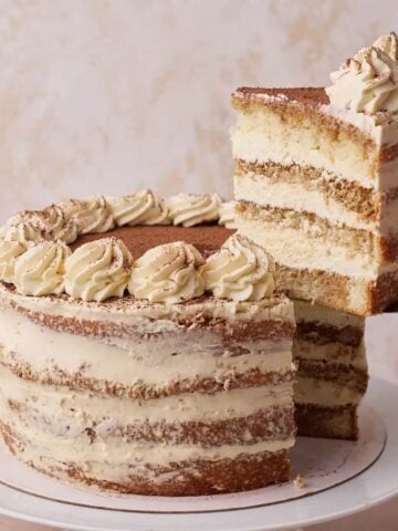 Tiramisu cake with a slice being taken out of it to show the layers of genoise sponge soaked in coffee and layered with mascarpone cream.