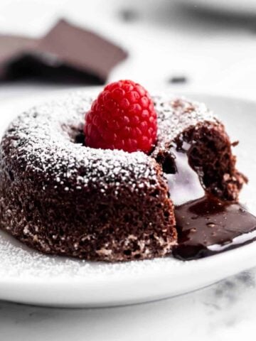 Chocolate lava cake on a plate with a bite taken out of it to reveal the molten chocolate middle oozing out.