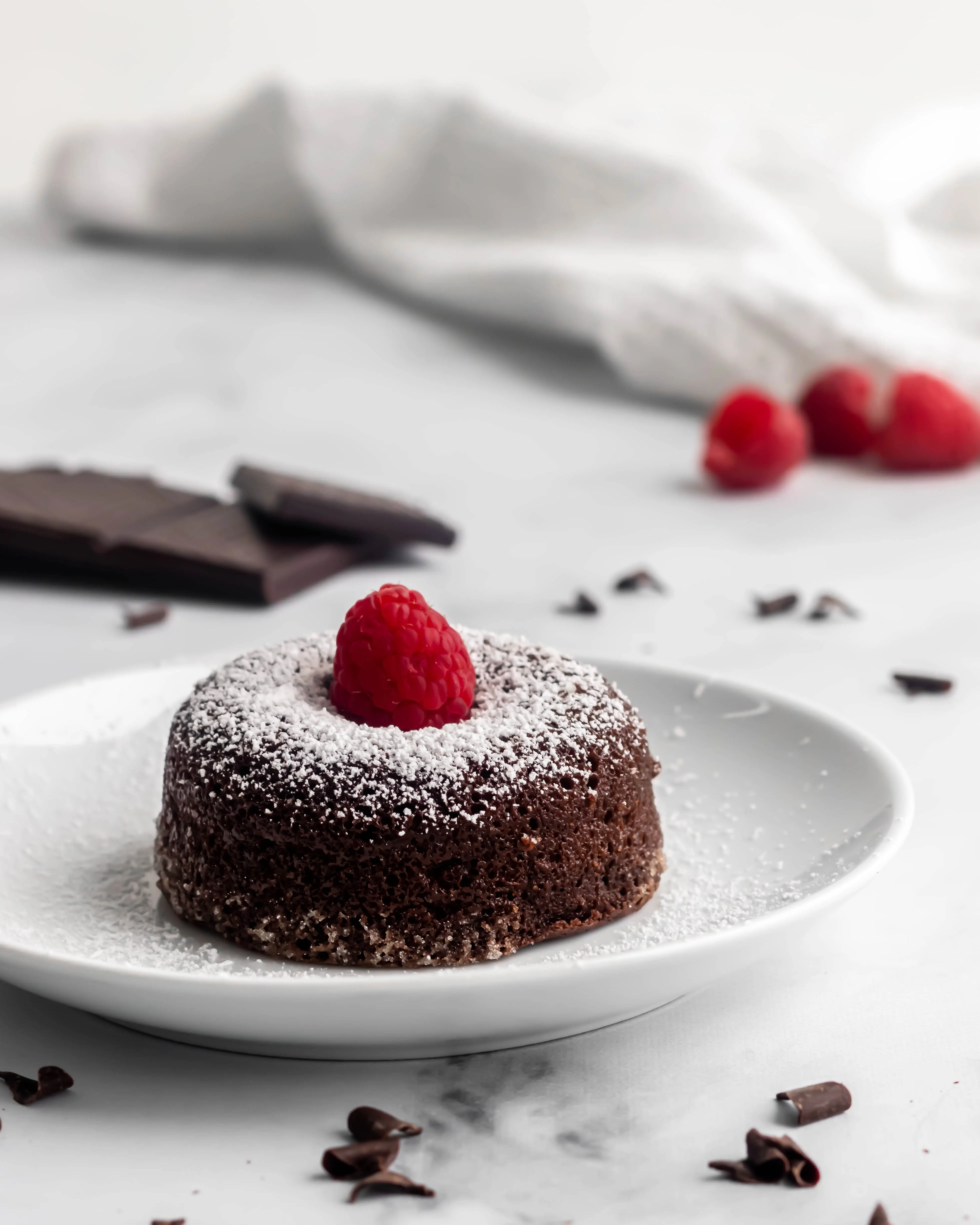 Chocolate lava cake on a plate with a single raspberry on top and a dusting of icing sugar. 