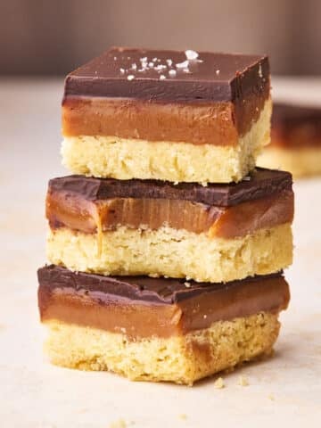 Three pieces of millionaire's shortbread in a stack, the middle one has a bite taken out of it to show the gooey caramel filling.