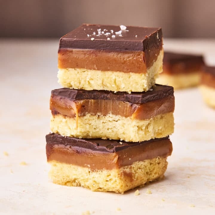 Three pieces of millionaire's shortbread in a stack, the middle one has a bite taken out of it to show the gooey caramel filling.