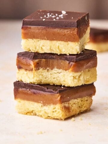 Three pieces of millionaire's shortbread in a stack, the middle one has a bite taken out of it to show the gooey caramel filling.