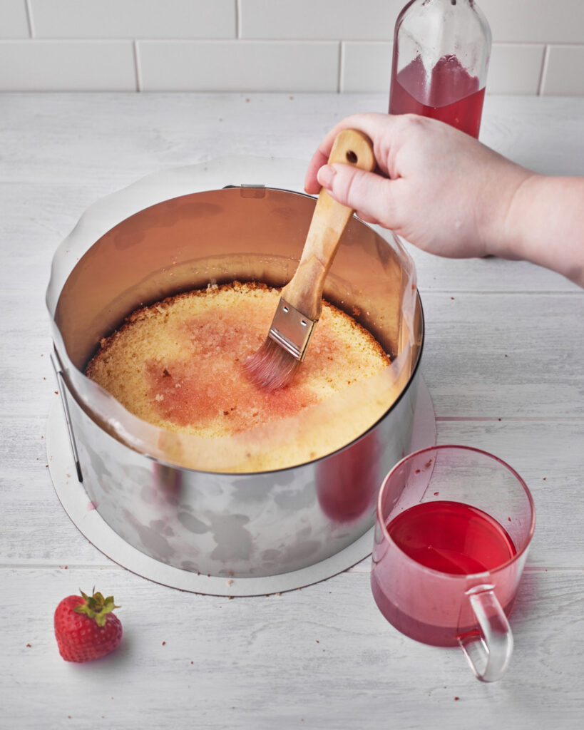 strawberry simple syrup being brushed onto genoise sponge cake.