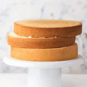 Three genoise sponge cakes stacked on top of each other on a cake stand.
