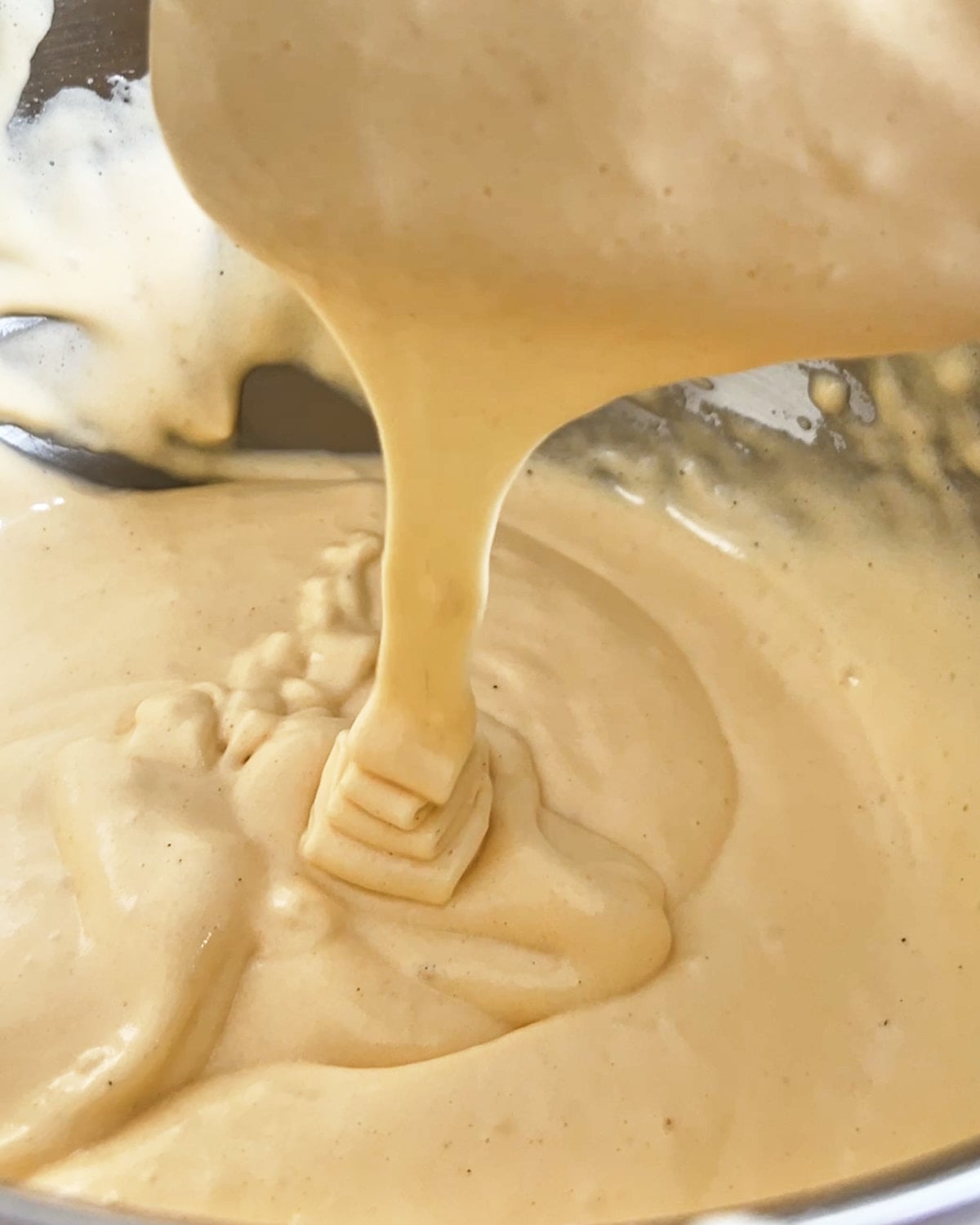 Genoise cake batter reaching the ribbon stage of mixing, flowing off the spatula in a ribbon shape.