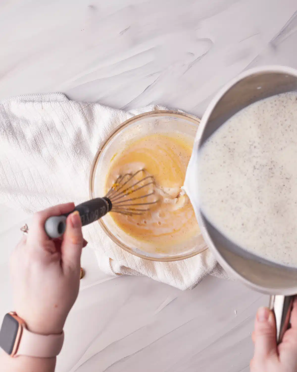 Drizzling warm milk into egg yolk mixture to make vanilla pastry cream.