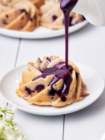 mini blueberry bundt cake with blueberry glaze being poured on top.