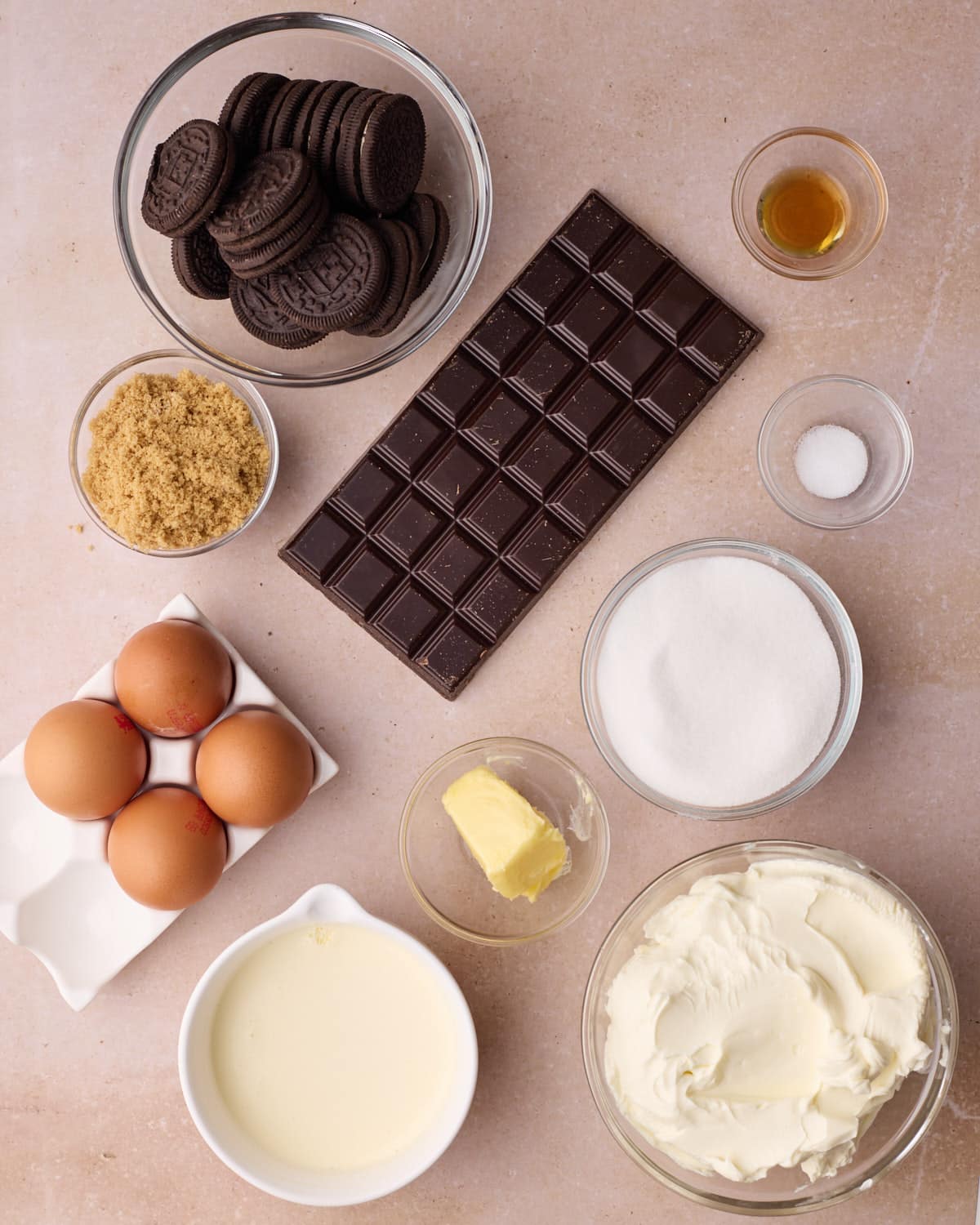 Ingredients to make chocolate cheesecake - including cream cheese, white sugar, light brown sugar, eggs, vanilla, salt, dark chocolate, and heavy cream.