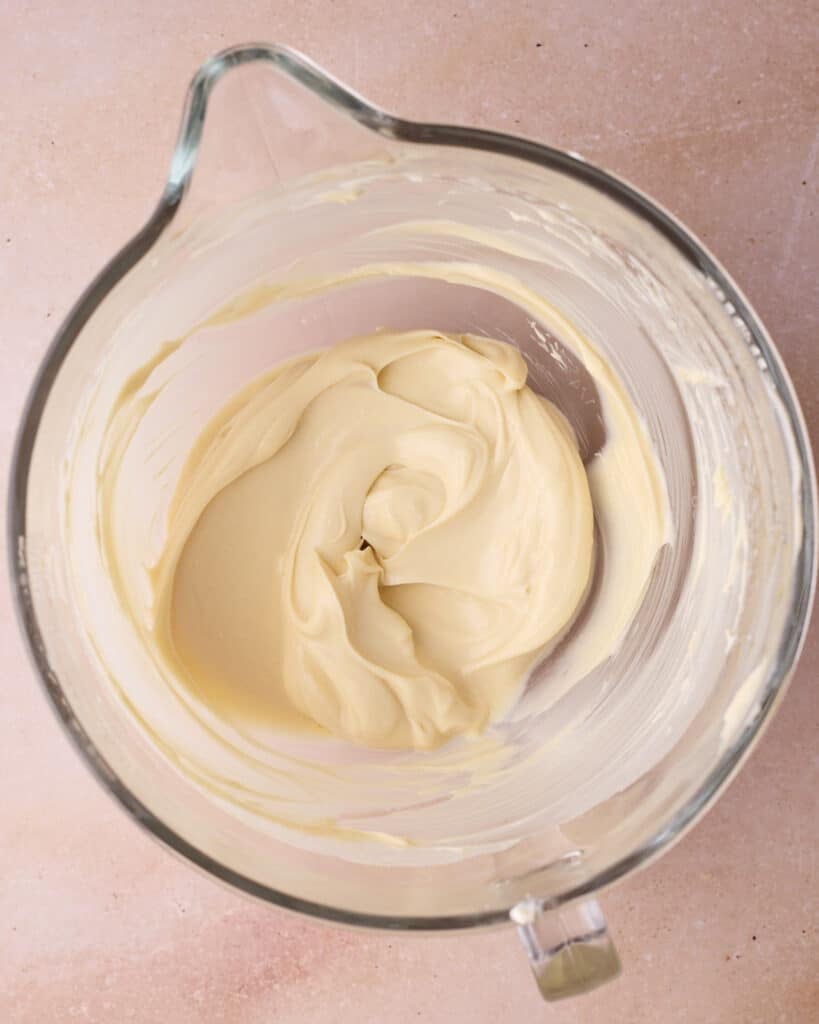 Cream cheese beaten together with sugar in a glass mixing bowl to make chocolate cheesecake batter.