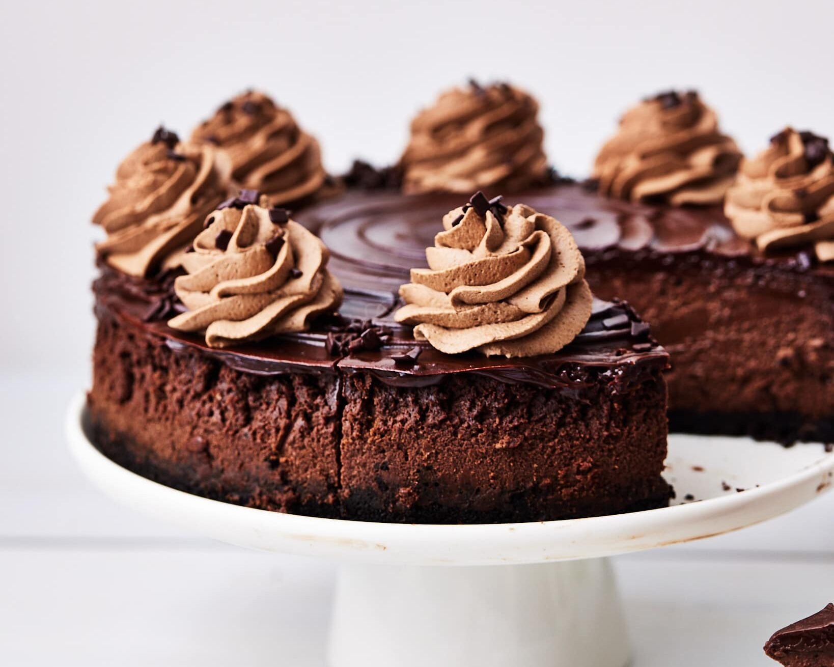 Baked chocolate cheesecake on a white cake stand with a slice taken out of it.