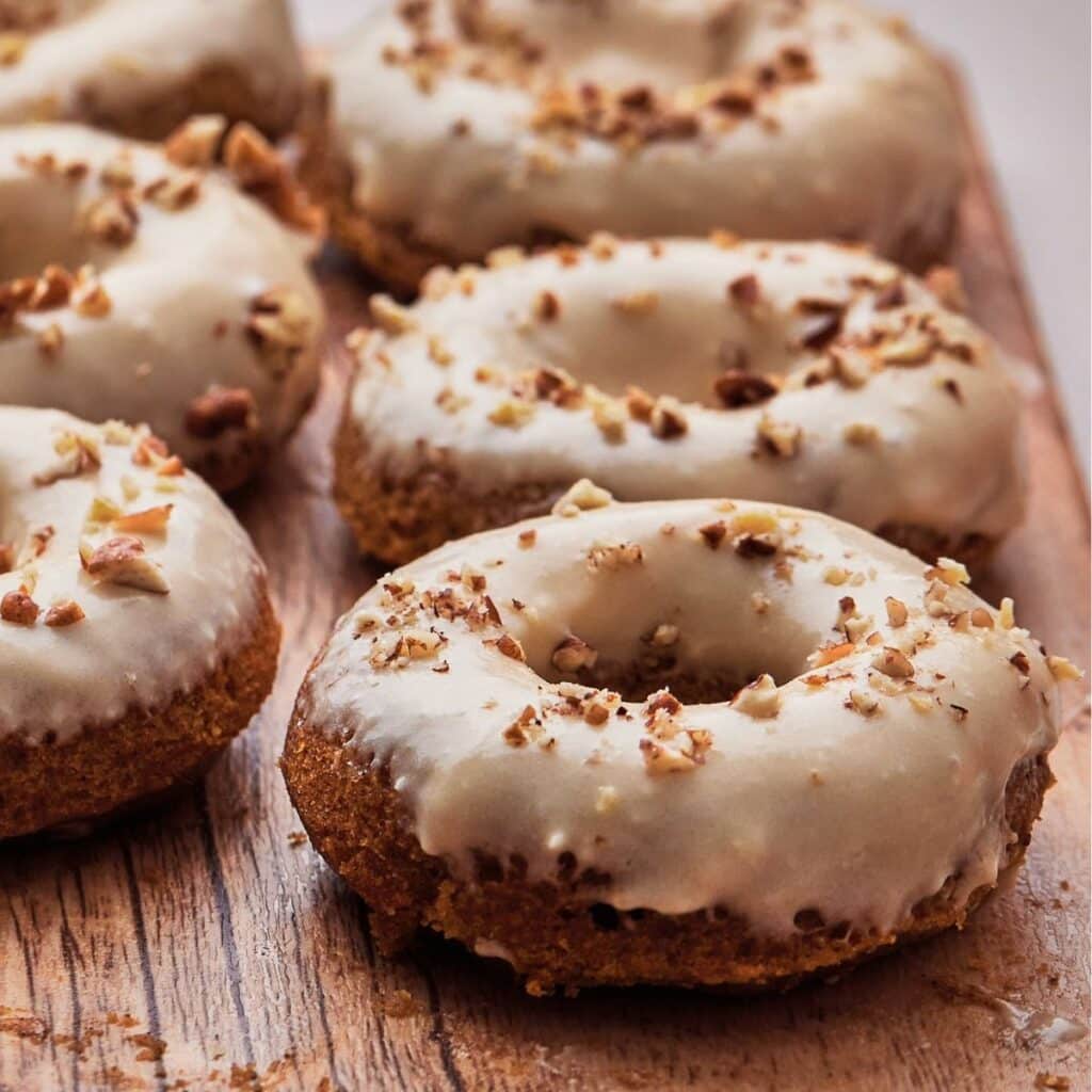 Pumpkin spiced donuts with a maple cream cheese icing and a sprinkling of pecans on top.