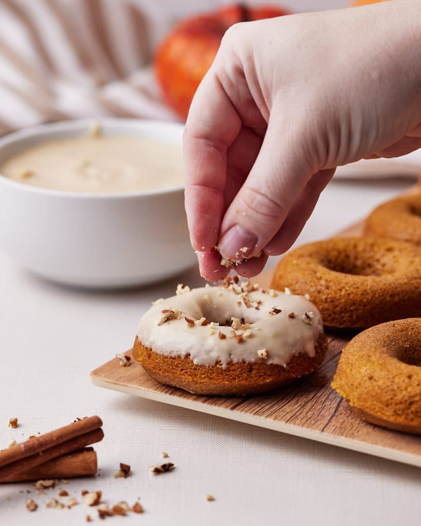 sprinkling pumpkin spice donut with chopped pecans