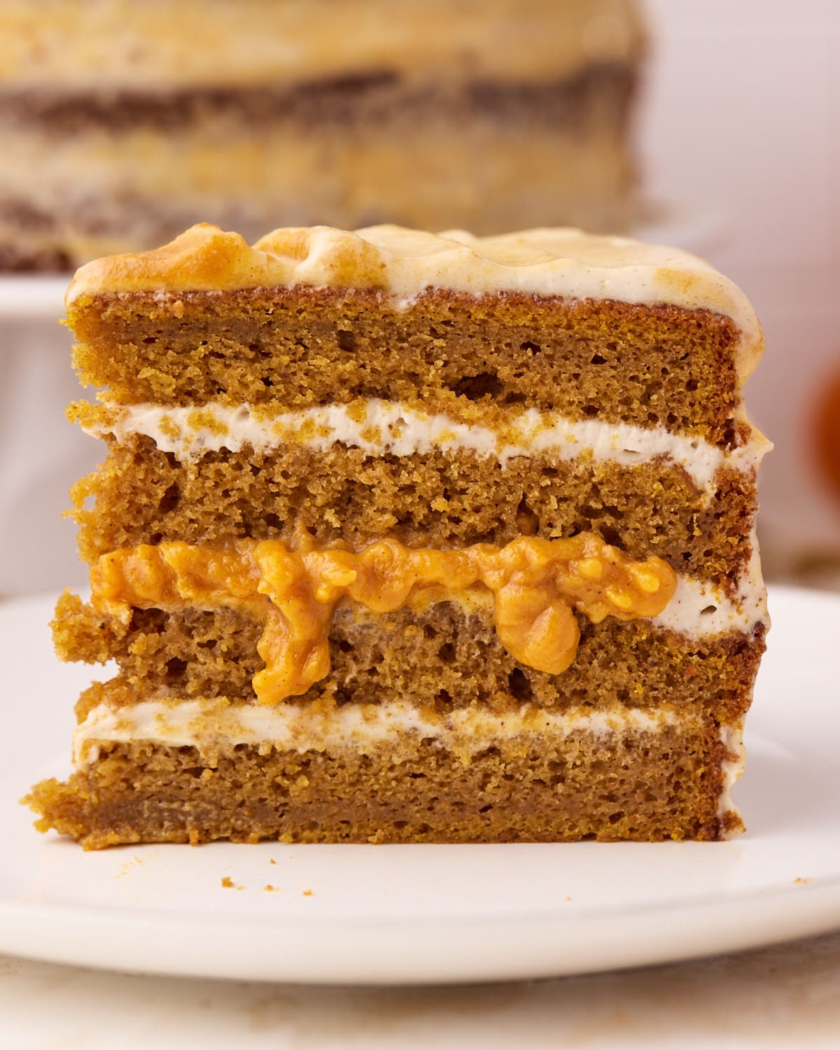 Slice of pumpkin cake from the side to reveal layers of cinnamon cream cheese frosting and pumpkin curd.