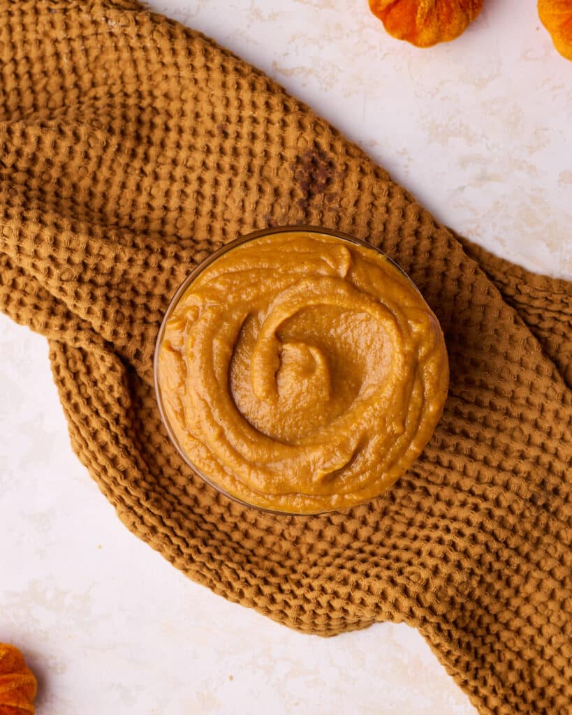 Pumpkin curd cooling in a glass bowl, sitting on top of an orange tea towel.