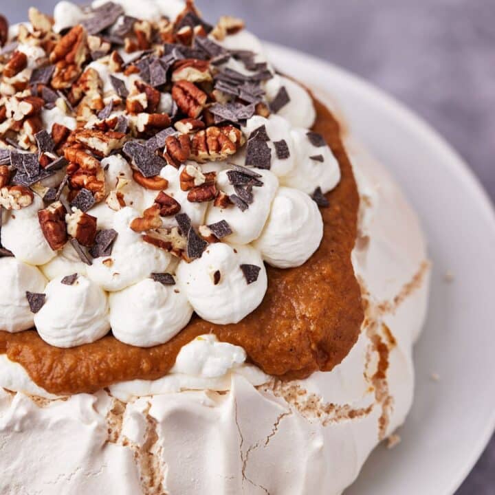 Pumpkin Pavlova, decorated with doots of whipped cream, and sprinkled with shaved chocolate and chopped pecans.