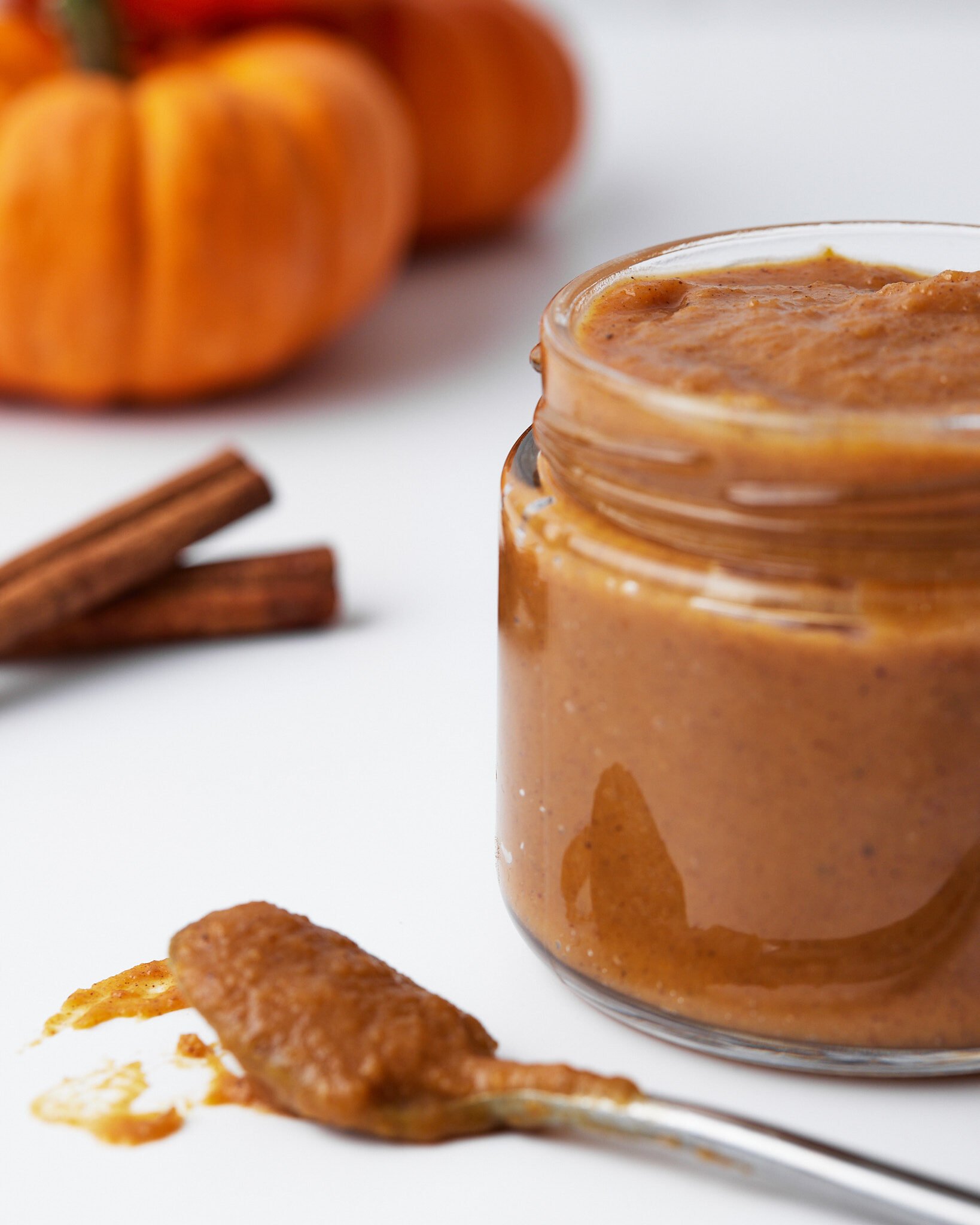 pumpkin curd in a glass jar, with cinnamon and pumpkins in the background. 