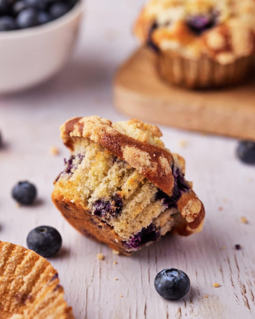 blueberry cream cheese muffin toppled over onto its side, loose blueberries around it